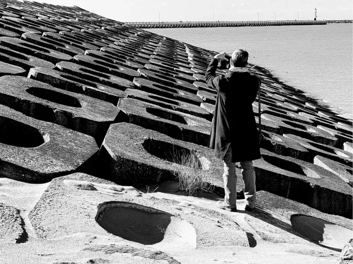 Man fotografeert de pier van Oostende vanop de betonblokken van een golfbreker, in zwart-wit