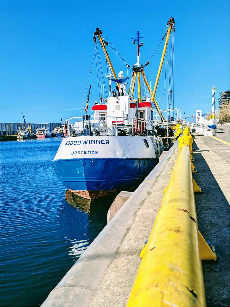 Blauw-witte vissersboot aan de kade in de haven van Oostende, met een gele leuning op de voorgrond