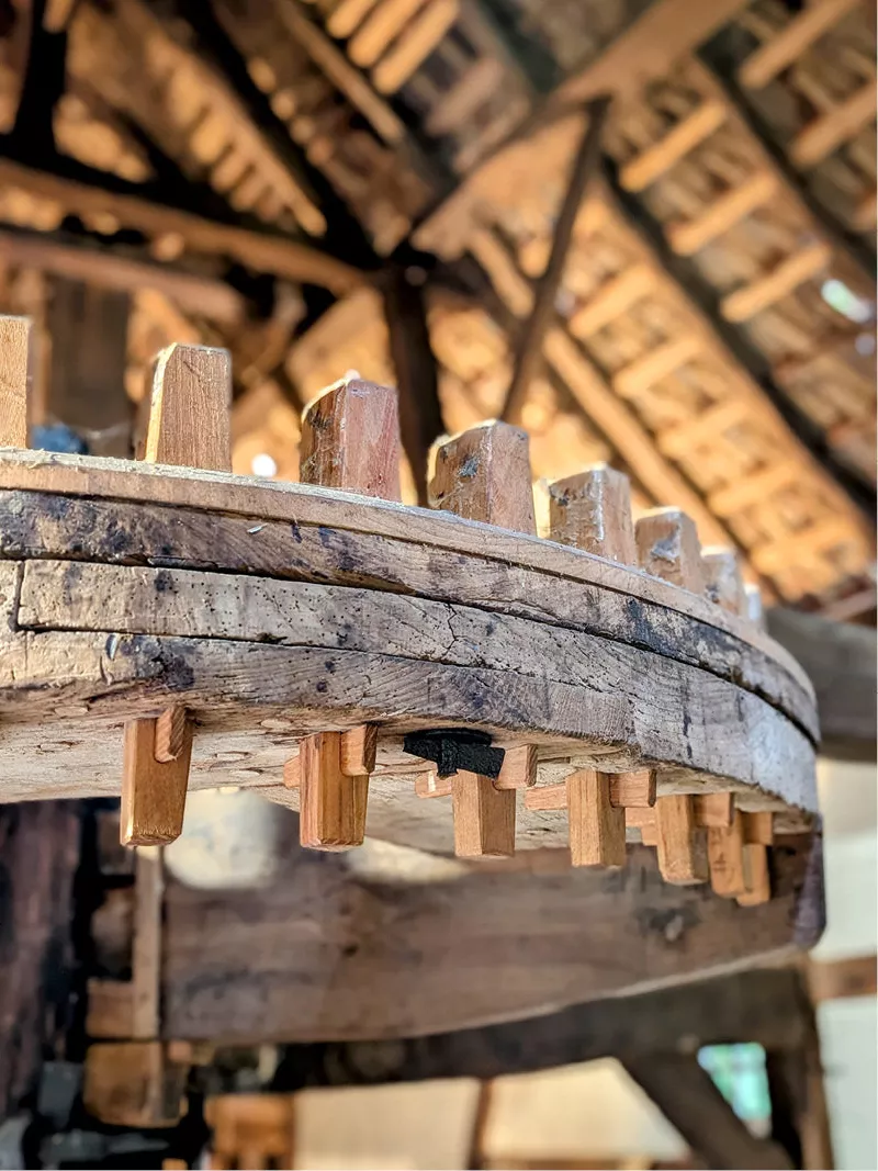 Houten kamwiel met tanden in een watermolen, met dakbalken op de achtergrond