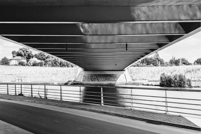 Onderkant van een betonnen brug over het water met een weg en leuning, in zwart-wit