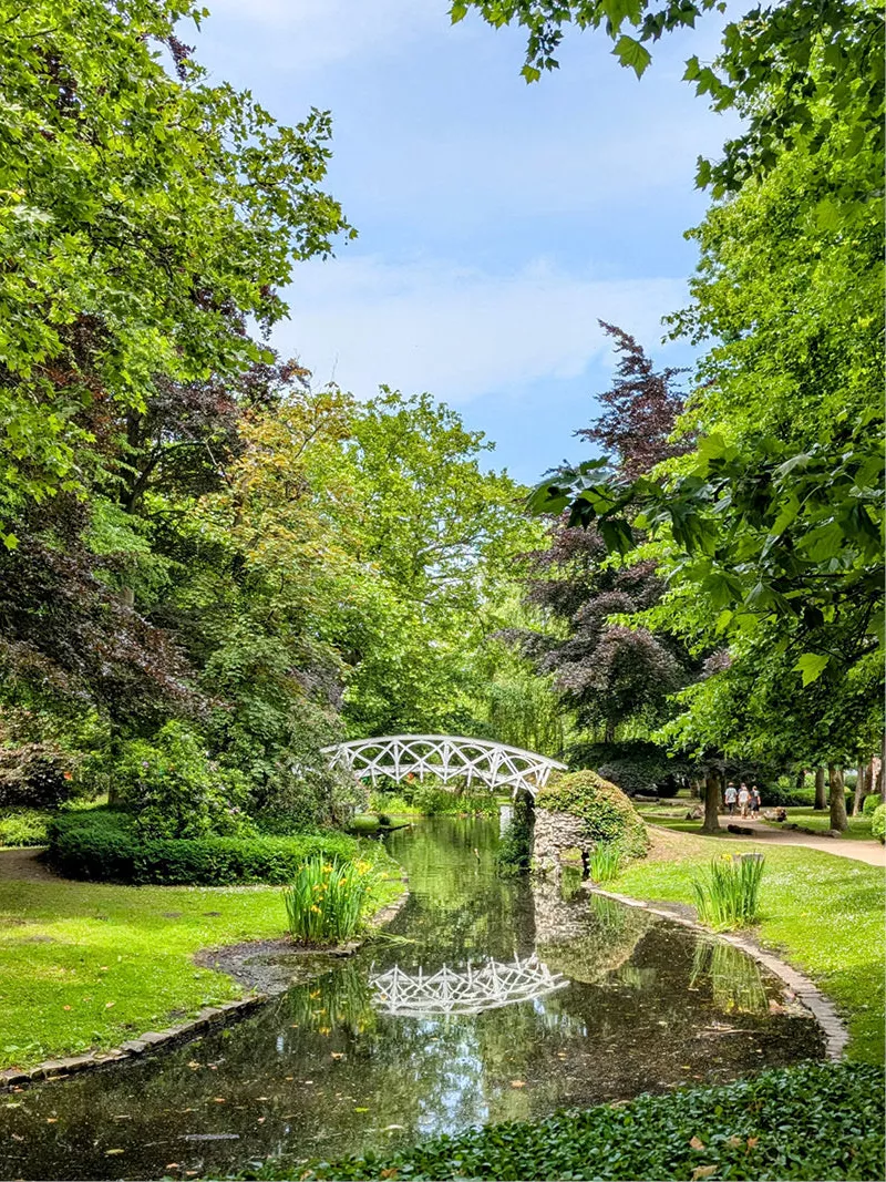 Witte sierbrug over een vijver in een groen stadspark, gespiegeld in het water