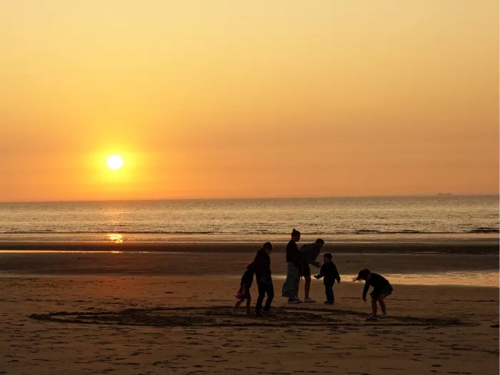 Silhouetten van kinderen en volwassenen die spelen op het strand bij zonsondergang