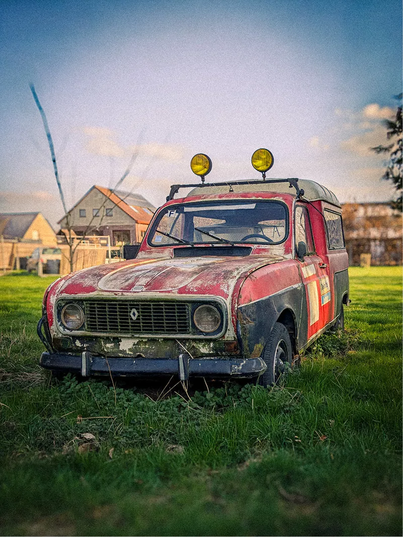 Oude roestige rode Renault 4 met gele daklampen in een grasveld