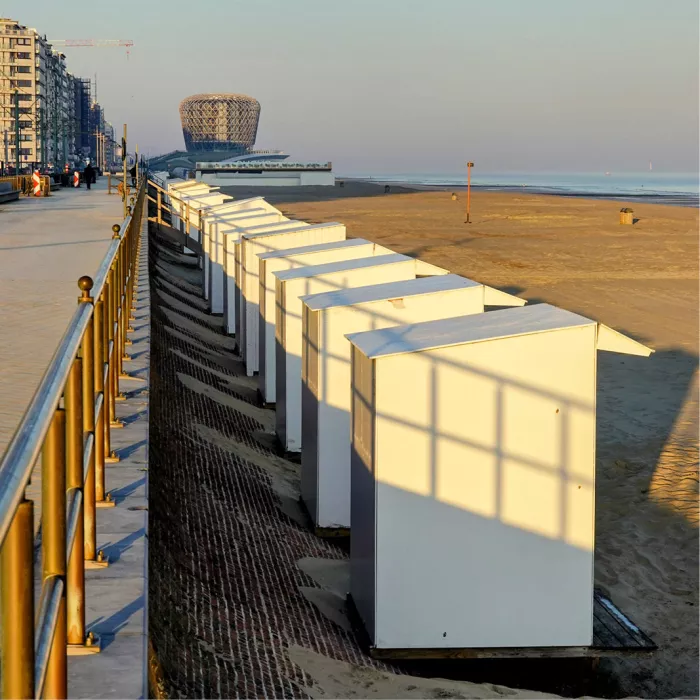 Witte strandcabines met schaduwlijnen naast de dijk, met het casino van Middelkerke erachter