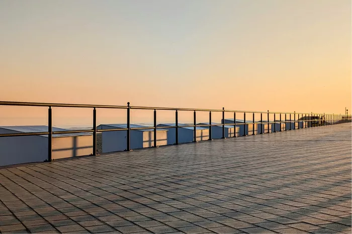 Strandcabines achter een zwarte reling op de dijk met schaduwkruisen bij zonsopgang