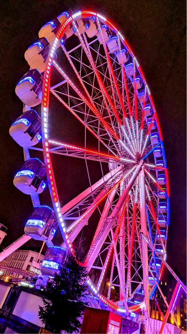 Verlicht reuzenrad met rode, witte en blauwe lichtjes en blauwe gondels tegen een donkere lucht