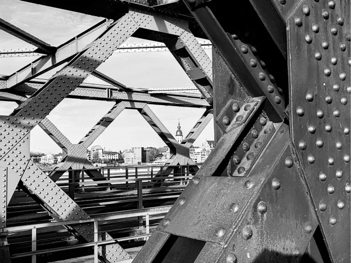 Doorkijk door de stalen vakwerkbalken met klinknagels van een brug naar een kerktoren, in zwart-wit