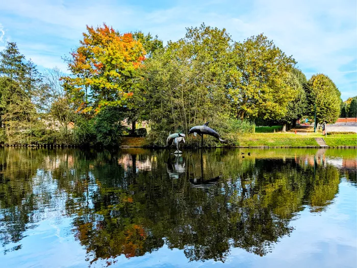 Vijver met dolfijnbeelden aan de oever en bomen die spiegelen in het water