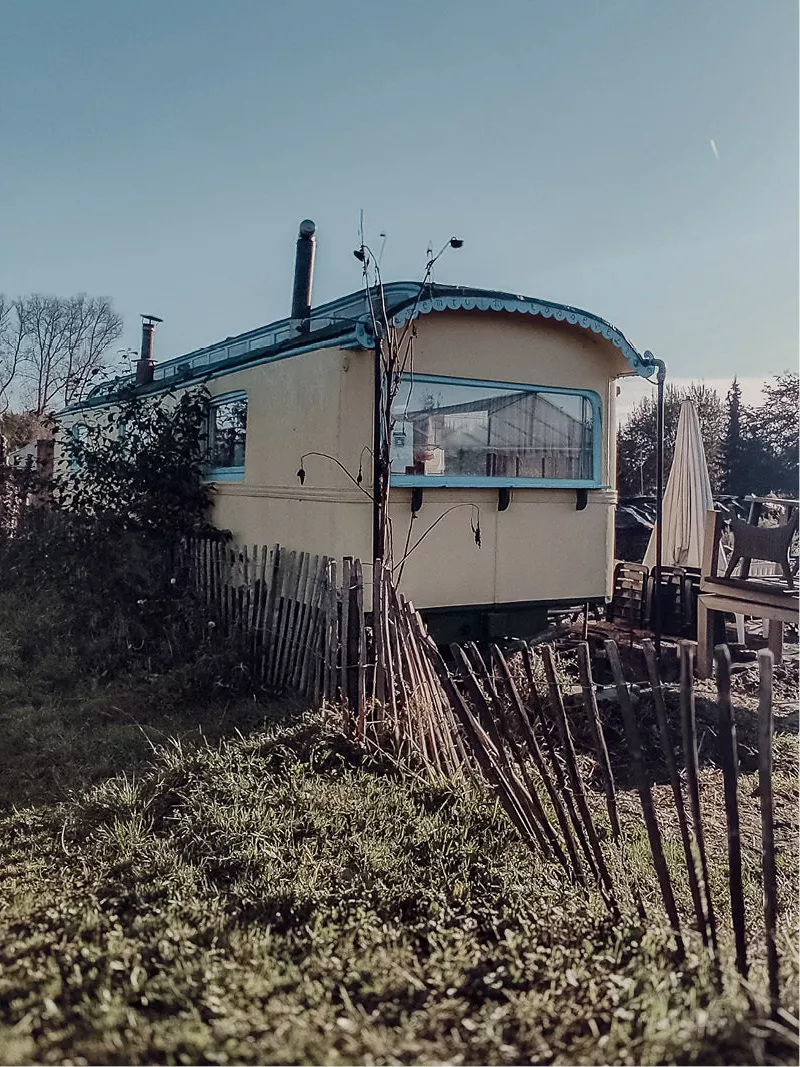 Retro stacaravan met gebogen dak achter een oud houten hekje in de tuin