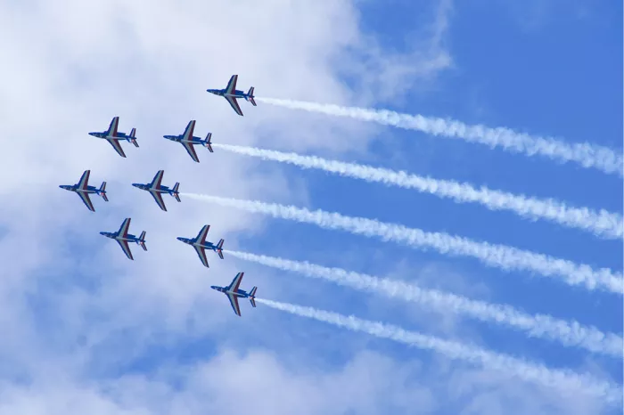 Acht straaljagers in formatie met parallelle witte rookstrepen tegen een blauwe lucht