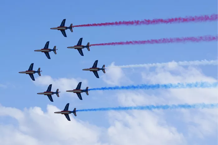 Straaljagers in formatie met rode, witte en blauwe rooksporen tegen een lichtblauwe lucht