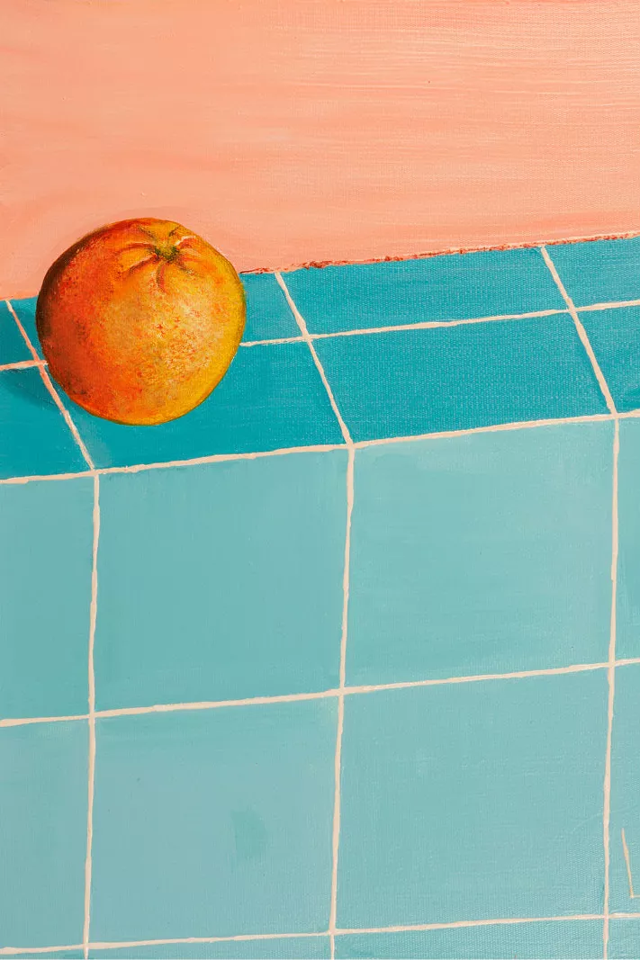 Appelsien op een tafel met turquoise tegels tegen een zalmroze muur