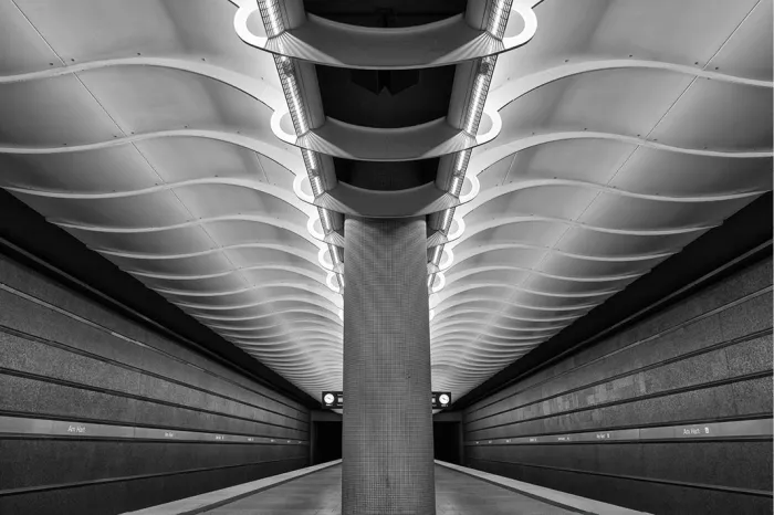 Symmetrisch metrostation met golvend wit plafond, lichtstroken en een betonnen zuil in het midden