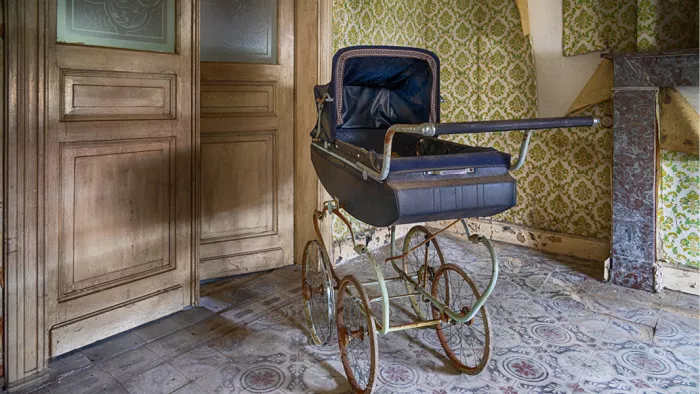 Antieke blauwe kinderwagen in een verlaten kamer met houten deuren en groen behang