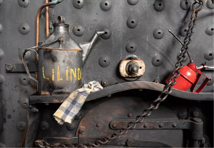 Oud oliekannetje, poetsdoek en rode oliespuit tegen een geklonken stalen locomotiefwand