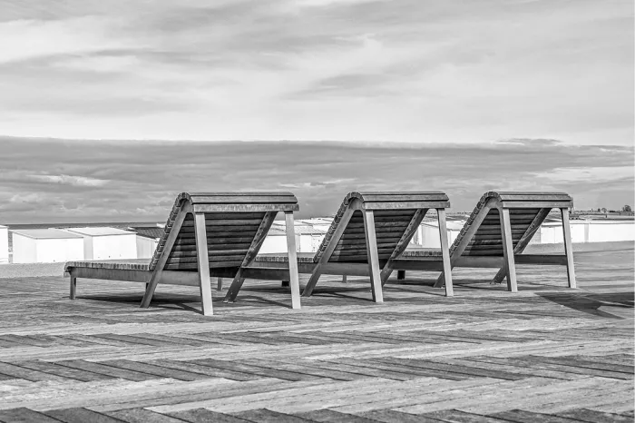 Drie houten ligzetels op een houten promenade met strandcabines en de zee
