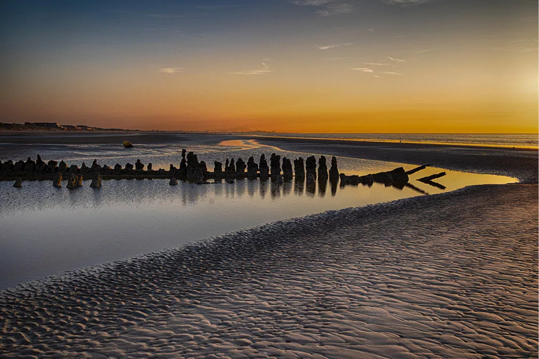 Houten resten van een scheepswrak als silhouet in een plas op het strand bij zonsondergang