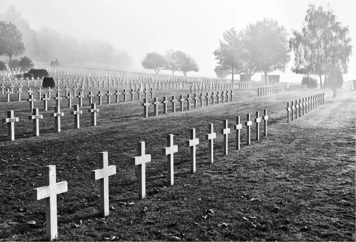 Rijen witte kruisen op een militair kerkhof met bomen in de mist