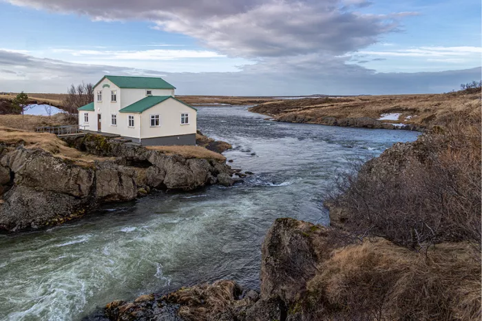Wit huis met groen dak op een rots boven een snelstromende rivier