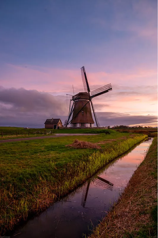 Windmolen aan het einde van een sloot met roze lucht en spiegeling, in staand formaat