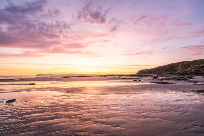 Zonsopgang aan een strand met roze en paarse wolken die spiegelen in het natte zand