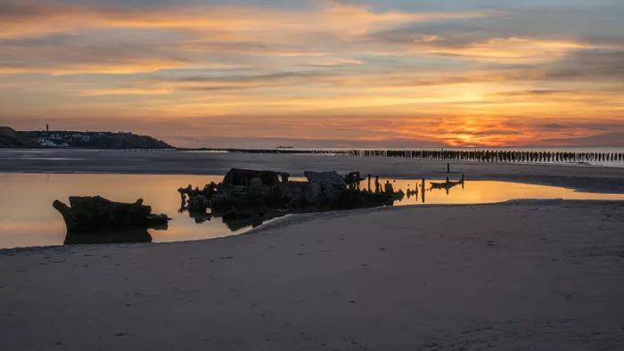 Strand na zonsondergang met oranje wolken, donkere resten in een plas en een rij strandpalen
