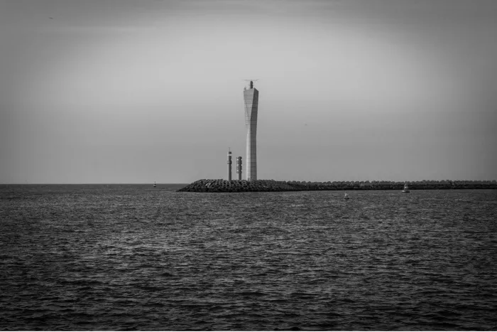 Slanke radartoren op een golfbreker boven een rimpelende zee onder een egale grijze lucht