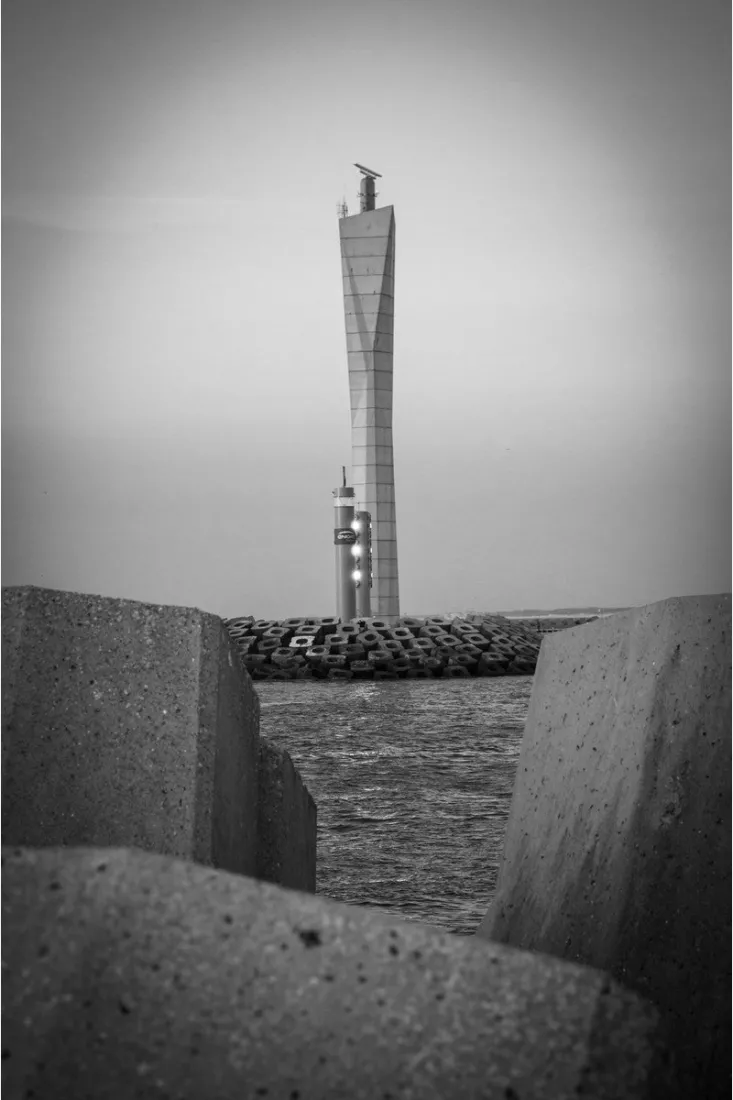 Radartoren aan de haven gezien tussen twee betonblokken, met water en een golfbreker