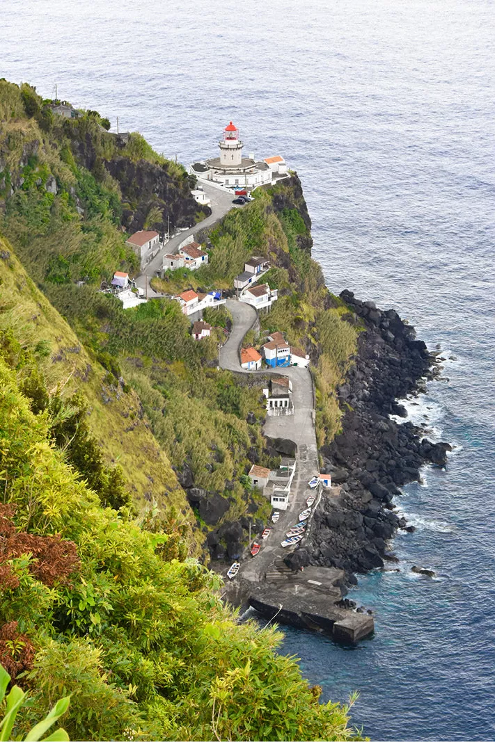 Vuurtoren op een groene klif boven de zee met een kronkelend weggetje en witte huisjes
