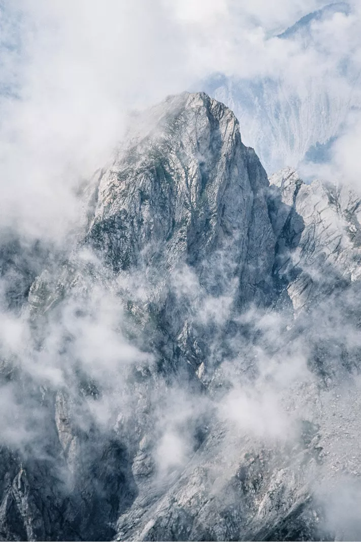 Rotsige bergtop met sneeuw tussen witte wolkenflarden en mist