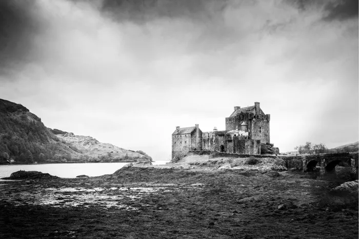 Kasteel Eilean Donan ligt bij laag water aan het loch, met de oude stenen brug en de heuvels van de Schotse Highlands op de achtergrond.