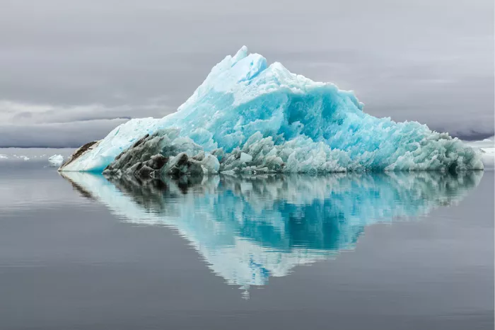 Turquoise ijsberg die met zijn spiegelbeeld een ruitvorm maakt op stil grijs water