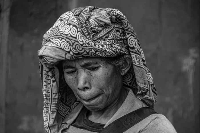 Oudere vrouw met een gedessineerde hoofddoek die naar beneden kijkt, in zwart-wit