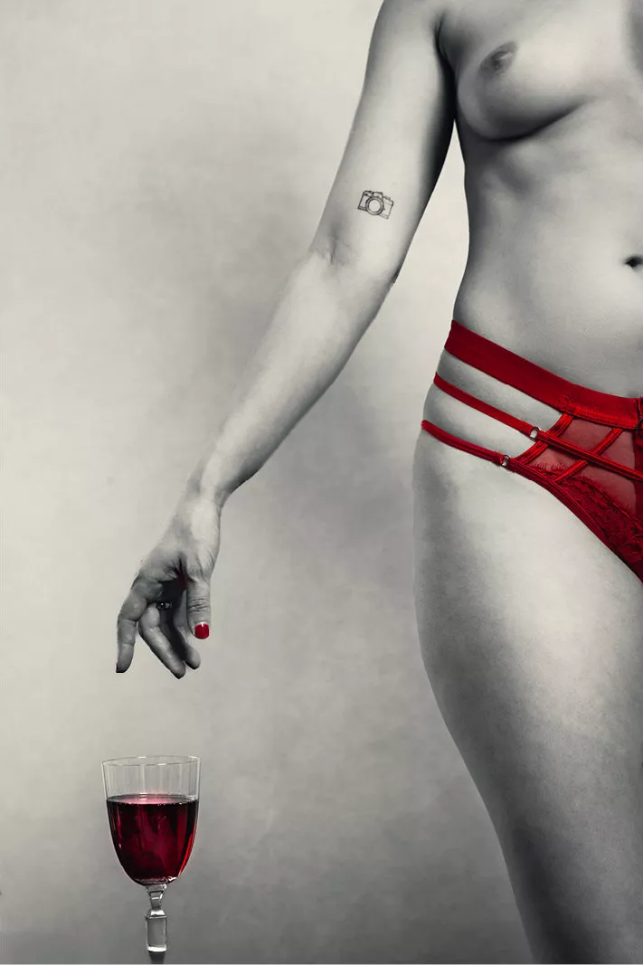 Vrouw in rood slipje met de hand boven een glas rode wijn, zwart-wit met rode accenten