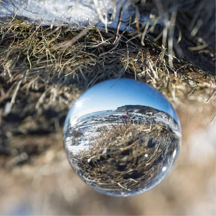 Glazen bol tussen droog gras en sneeuw, met de omgeving en de blauwe lucht omgekeerd in de bol