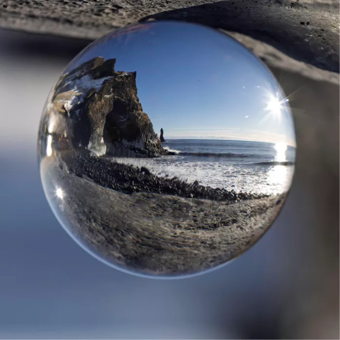 Glazen bol met daarin het zwarte strand, donkere rotsen, branding en een stralende zon