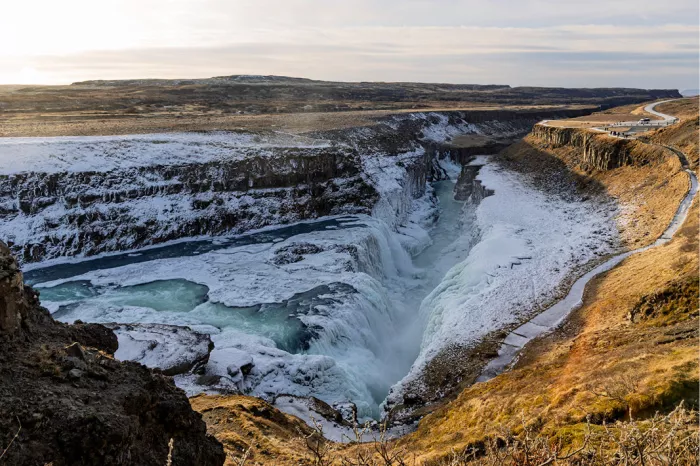 Gedeeltelijk bevroren waterval in een diepe kloof met sneeuw, blauwgroen water en goudbruin gras