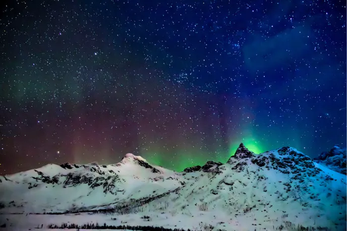 Groen en rood noorderlicht boven besneeuwde bergtoppen onder een sterrenhemel