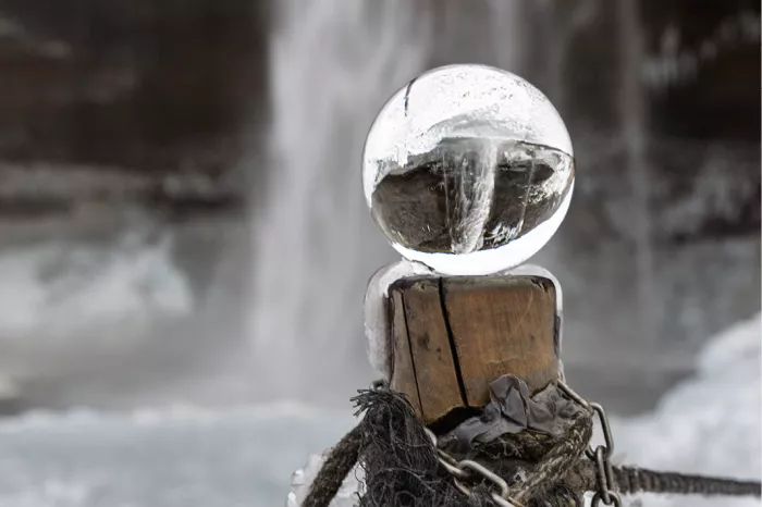 Glazen bol op een houten paaltje met daarin een bevroren waterval, met de waterval wazig erachter