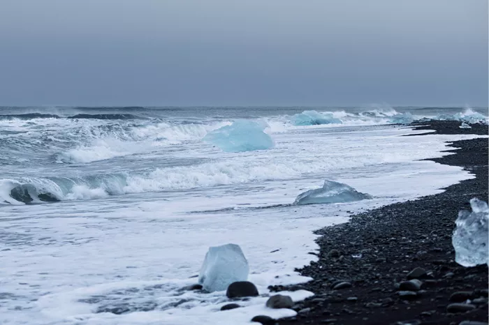 IJsblokken in het schuim van witte golven langs een strand met zwarte kiezels