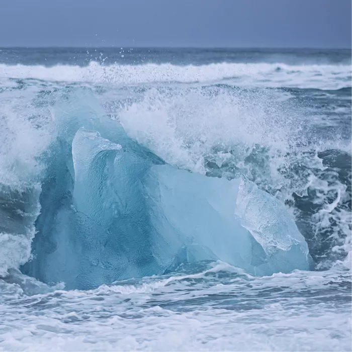 Golf die opspat tegen een groot turquoise ijsblok op het strand