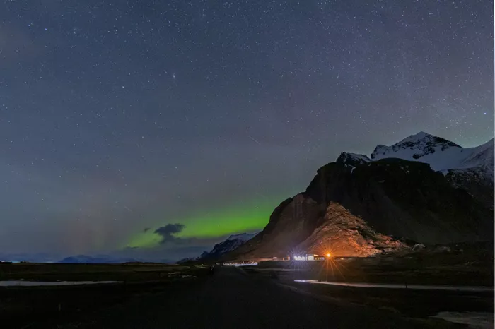 Lege weg in het donker met een sterrenhemel, groen noorderlicht en een verlichte berg