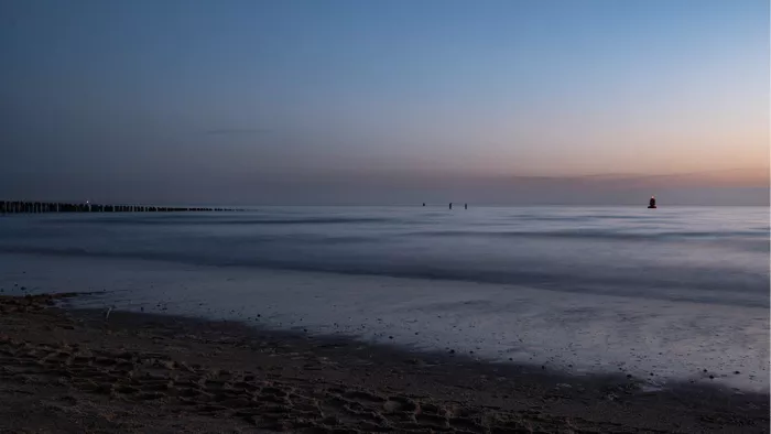 Strand en zee tijdens het blauwe uurtje met paalhoofden en een kleine rode lichtboei