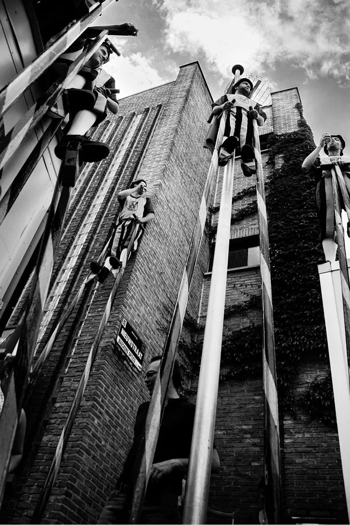 Steltenlopers die met hun stelten tegen een hoge bakstenen gevel leunen, van onderen gezien