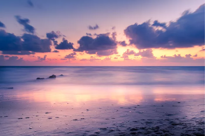 Strand bij zonsondergang met paarse wolken, roze horizon en zacht wazige zee
