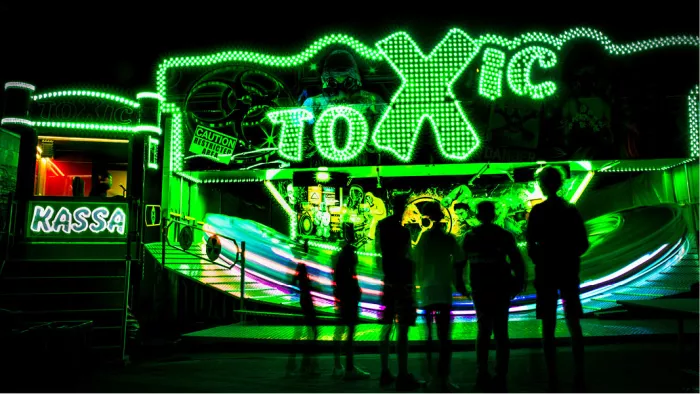 Groen verlichte kermisattractie Toxic bij nacht met silhouetten van toeschouwers