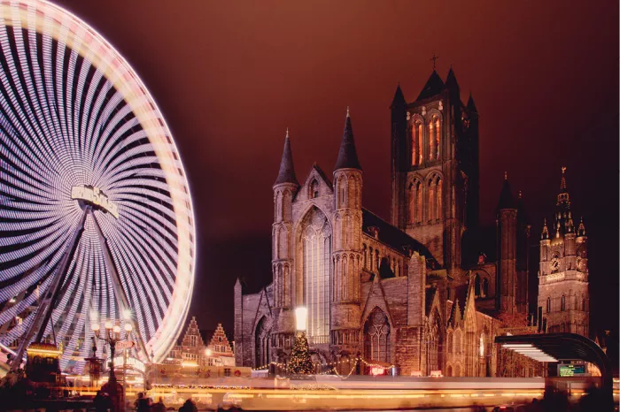 Draaiend reuzenrad in lichtstrepen naast de verlichte Sint-Niklaaskerk in Gent bij nacht