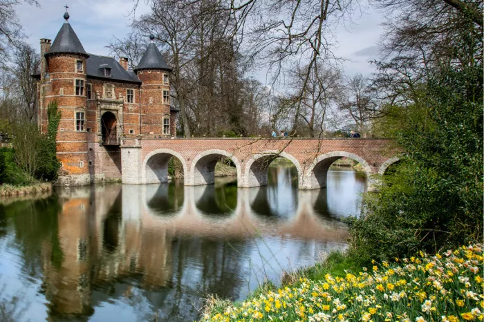Bakstenen waterburcht met boogbrug over de gracht en bloeiende narcissen op de oever