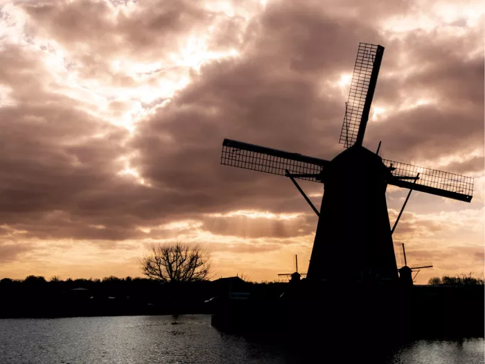 Silhouet van een windmolen aan het water onder een dramatische wolkenlucht bij valavond
