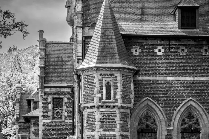 Spits torentje, bakstenen muren en spitsboogramen van een kasteel in zwart-wit